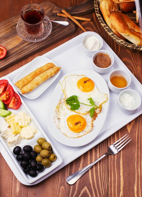 Turkish breakfast with fried eggs, tomato, cucumber, cheese varieties, black green olives, honey, jam, cream cheese, galeta bread and glass of tea 