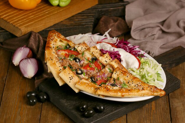 Turkish pide with olives and tomatoes on a wooden board