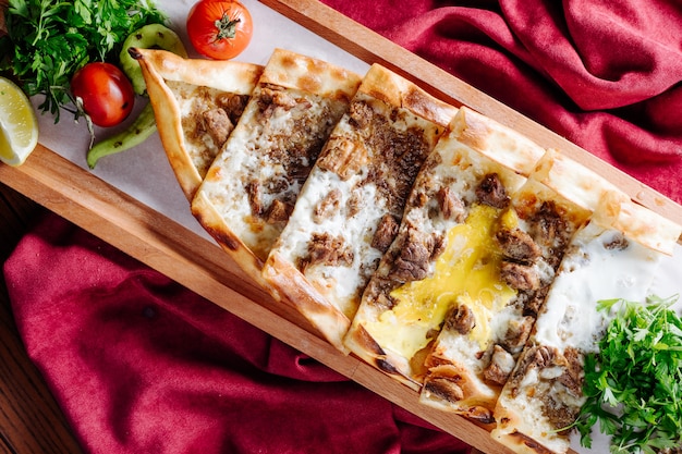 Turkish traditional lahmacun with meat and cheese stuffing served inside wooden platter.