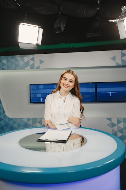 Free photo tv present at studio preparing for new broadcasting. smiling girl in white shirt sitting at table .