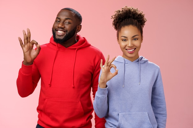 Two african-american skilful coworkers professionals assured friend everything perfect smiling broadly delighted nodding agree approval gesture show okay ok not bad choice sign, pink background