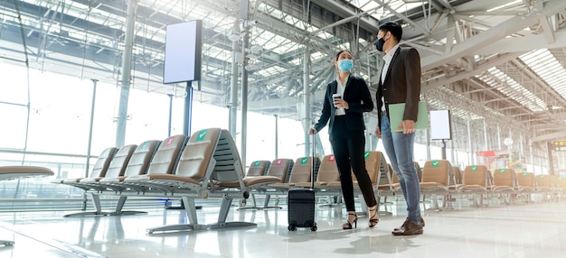 Free photo two asian business partners with face mask protection social distancing new normal lifestyle business travellers walking in airport with luggage