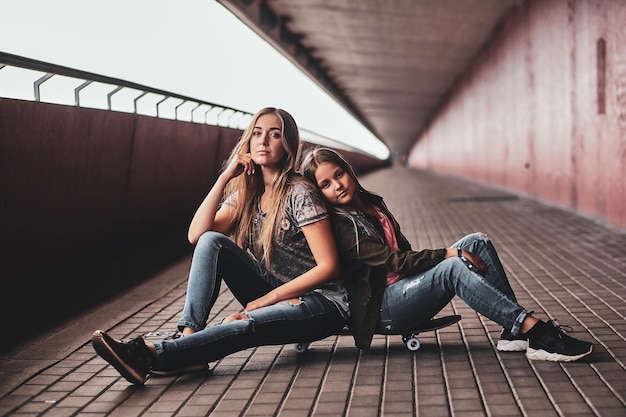 Free photo two attractive friendly teenagers are sitting on the skateboard in long tunnel.