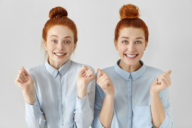 Free photo two attractive happy young redhead women with hair knots wearing light-blue shirts