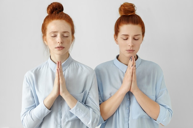 Free photo two attractive redhead student girls with hair buns, wearing identical shirts, posing at white wall