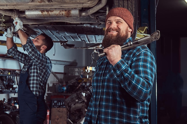 Free Photo two bearded brutal mechanics repair a car on a lift in the garage. repairing car suspension in a service station.