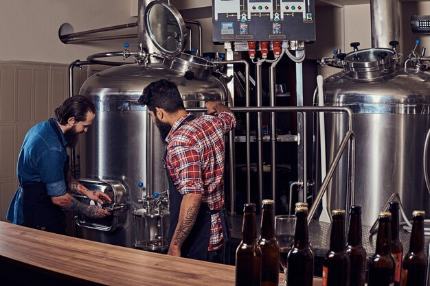 Two bearded hipster males in an apron working in the brewery factory.