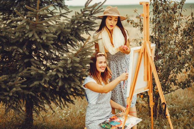 Two beautiful girls drawing in a field