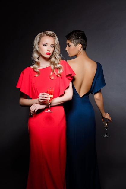 Two beautiful women in evening dresses posing, holding champaign glass