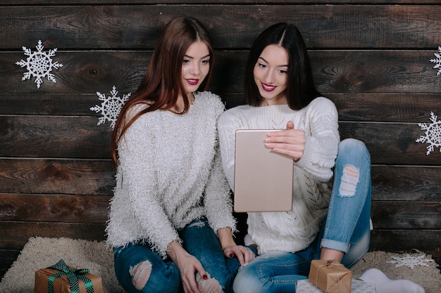 Free photo two beautiful women sitting on the floor with a tablet, between gifts for christmas