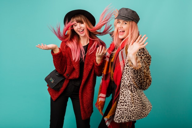 Two beautiful women in stylish faux fur coats and wool scarf posing on turquoise wall