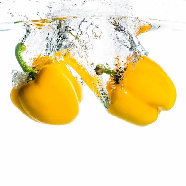 Two bell pepper falling into the water splash on white background