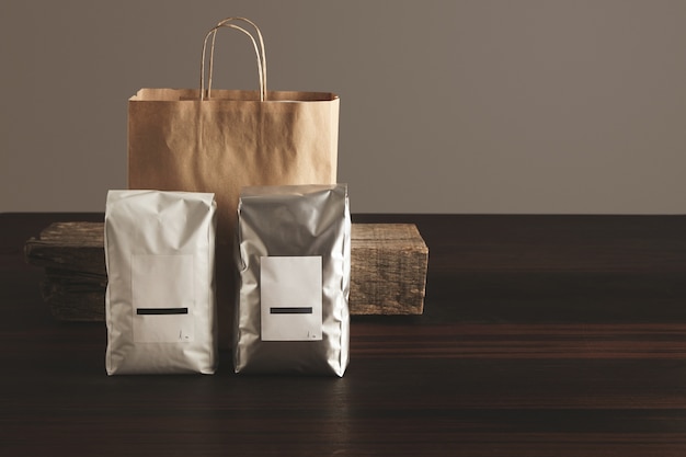 Two big hermetic packages with blank labels presented in front of craft paper bag and rustic wooden brick on red table