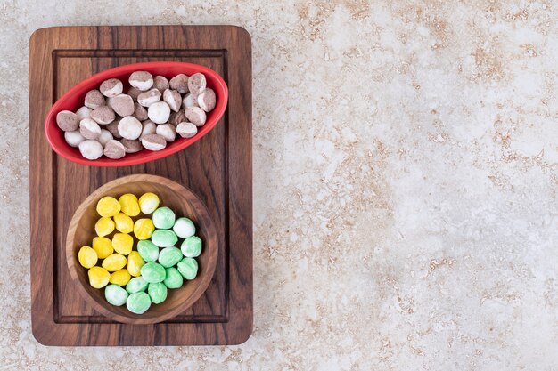 Two bowls of colorful candies on wooden board