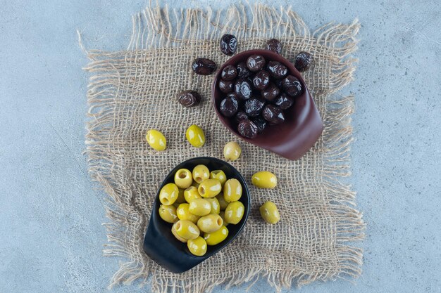 Two bowls of green and black olives on marble surface