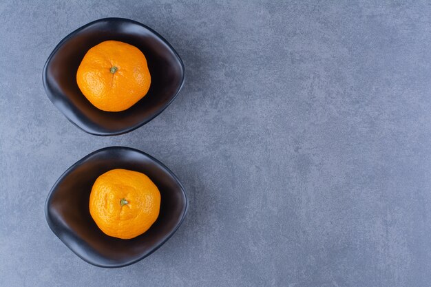 Two bowls of oranges, on the dark surface