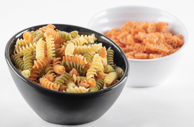 Two bowls of raw pasta on white.