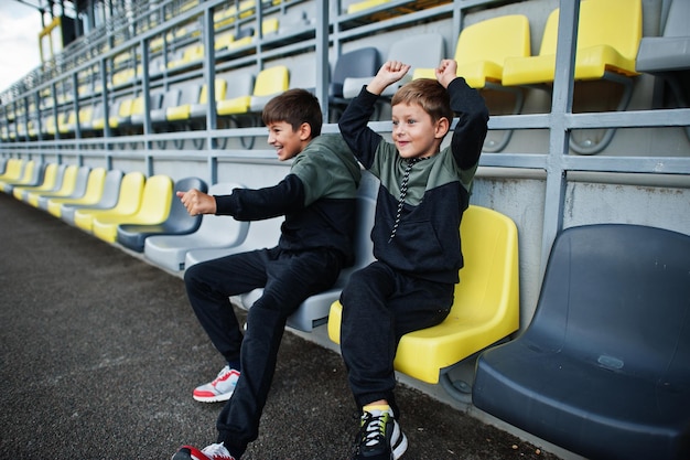 Free photo two brothers support their favorite team sitting on the sports podium at the stadium