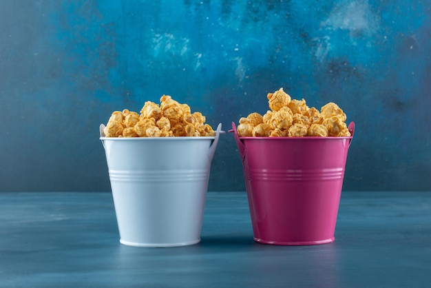 Two buckets filled with caramel coated popcorn on blue