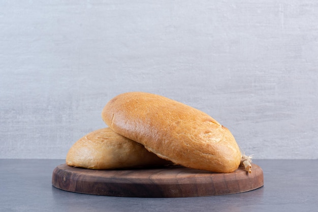 Two buns and a single wheat stalk on a wooden board on marble background. High quality photo