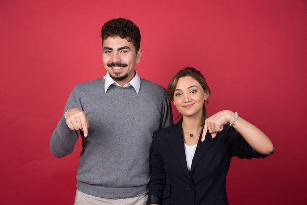 Two business partners giving pointing at down side on red wall