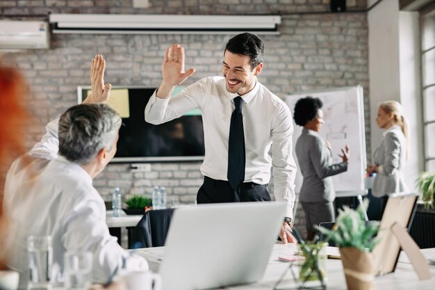 Two businessmen congratulating to each other on successful job and giving highfive Focus is on young businessman