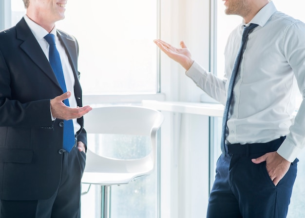 Free photo two businessmen gesturing while having conversation in office