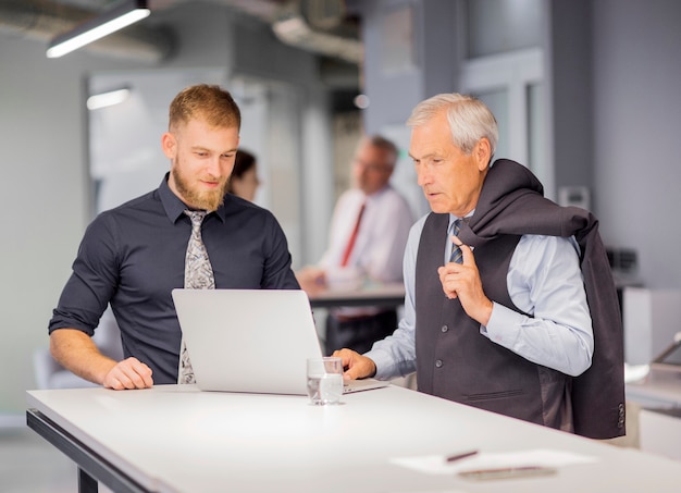 Free photo two businessmen standing near the table looking at laptop in the office