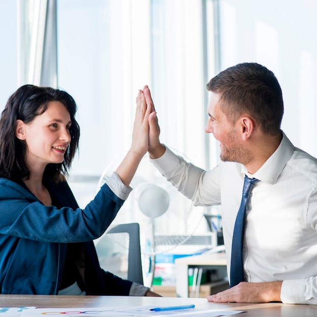 Free photo two businesswoman and businessman giving hi-five across the table