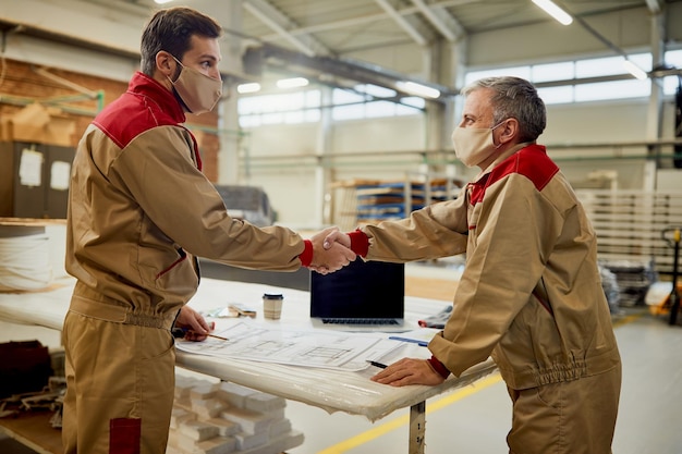 Two carpenters with face masks congratulating each other on successful project in a workshop