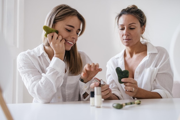 Free photo two caucasian blonde women of different ages are tasting cosmetic product while sitting on white background. skin care and hydration concept