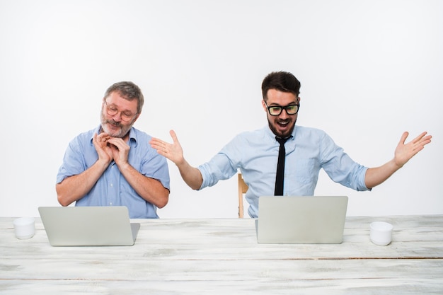 Free photo the two colleagues working together at office on white  background. both are looking at the computer screens. both surprised. concept of positive emotions and good news