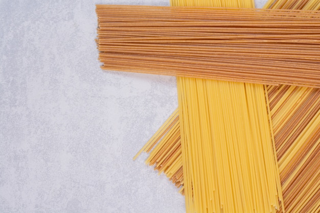 Two colors of raw spaghetti pasta on white surface