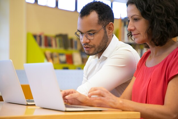 Two concentrated students talking and looking at laptop at library