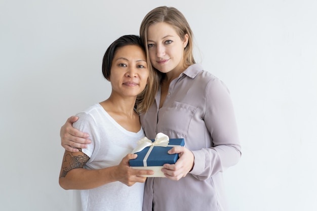 Two content women embracing and holding gift box