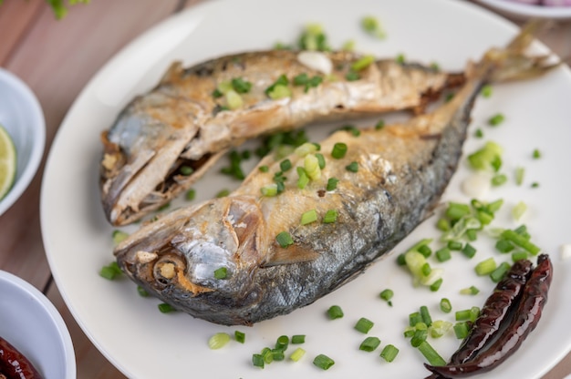 Two cooked mackerel, placed in a white dish, sprinkled with spring onions.