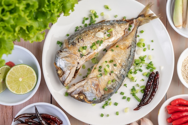 Two cooked mackerel, placed in a white dish, sprinkled with spring onions.