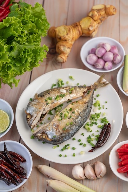 Free photo two cooked mackerel, placed in a white dish, sprinkled with spring onions.