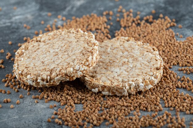 Two crispbread and uncooked buckwheat on marble surface