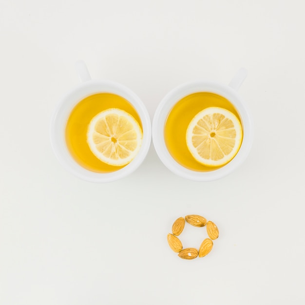 Free photo two cup of ginger tea with lemon slice and almonds isolated on white backdrop