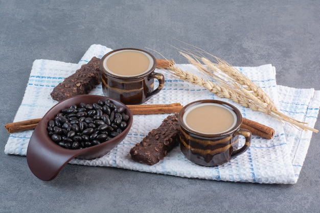 Two cups of coffee with sheet of paper and chocolates on tablecloth.