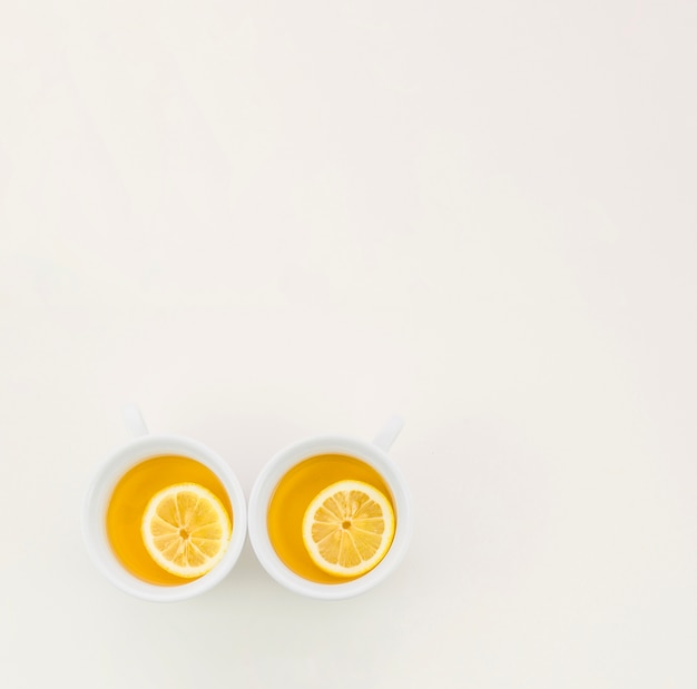 Two cups of green tea with lemon slice on white backdrop