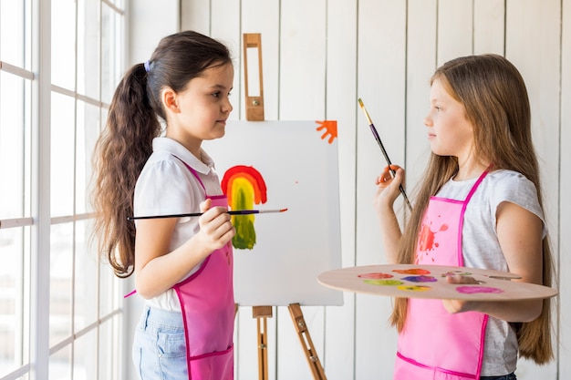 Free photo two cute girls painting on the canvas looking at each other