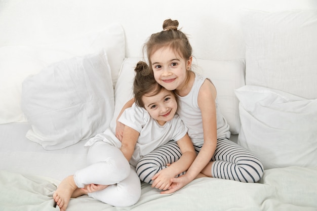 Free photo two cute little sister girls are cuddling on the bed in the bedroom.