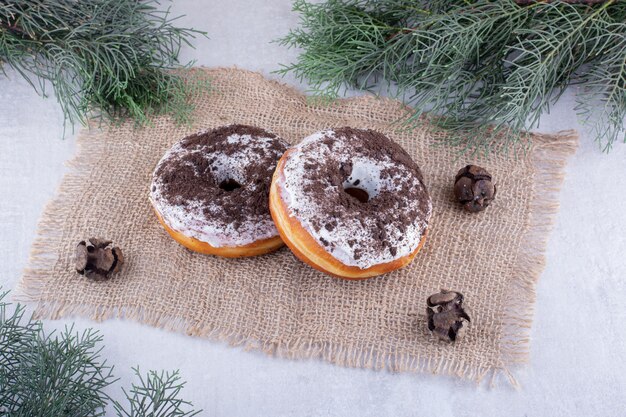 Two donuts on a piece of cloth among pine branches on white background.