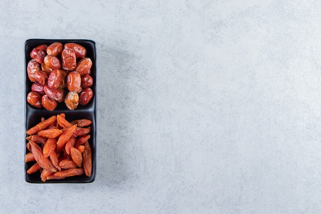 Two dried organic fruits on black plate on stone background.