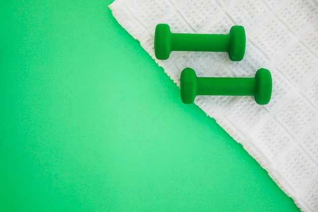 Two dumbbells on white cloth over green background