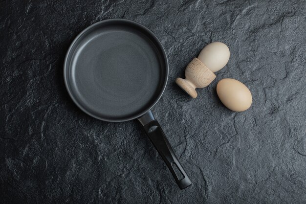 Two egg and black frying pan on black background.