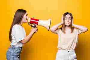 Free photo two excited young women girls friends in casual t-shirts denim clothes posing isolated on yellow wall. people lifestyle concept. mock up copy space. scream in megaphone, spreading hands