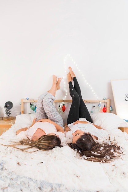 Two female friend lying on bed with their legs up